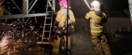 Strażacy gaszą pożar rurociągu. Teren akcji oświetla najaśnica. W okolicach rurociągu silne zadymienie