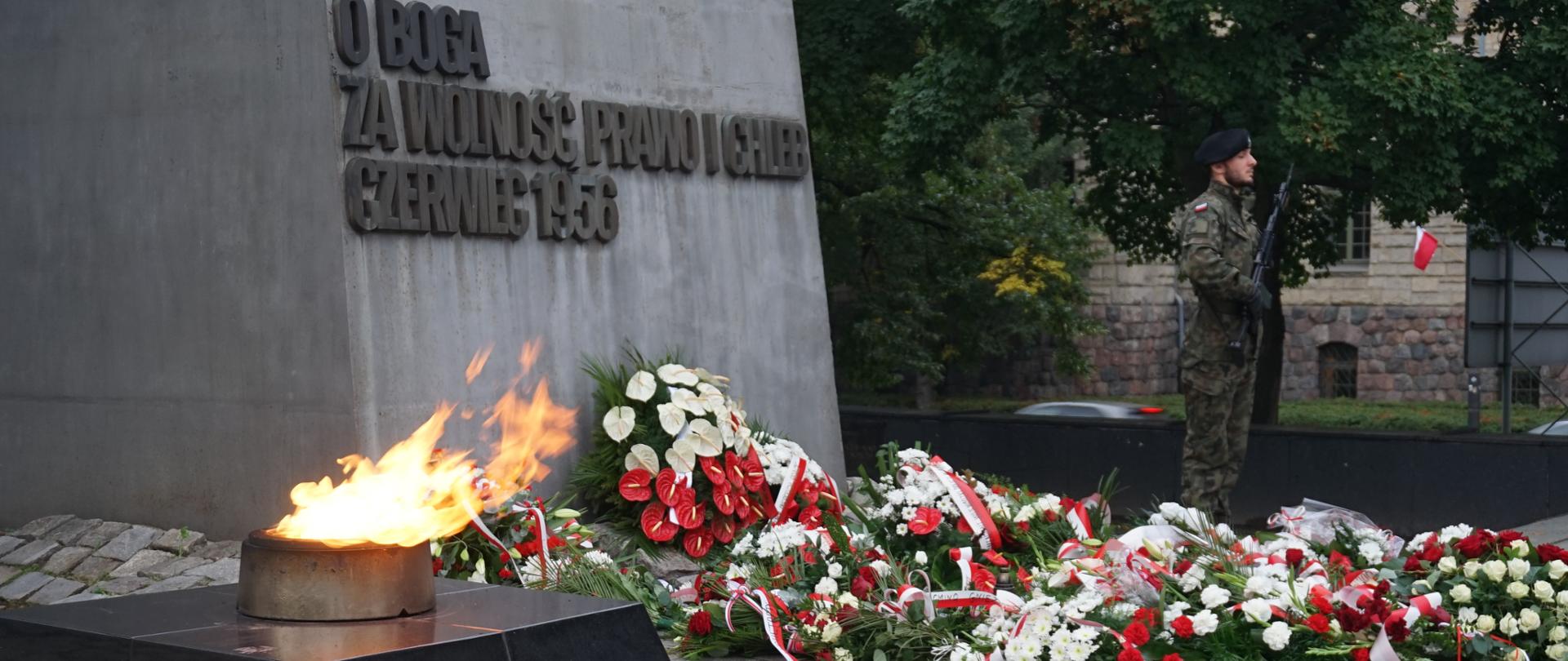 duzy znicz, wieńce biało czerwonych kwiatówpod pomniikiem na którym widnieje napis o boga za wolność prawo i chleb czerwiec 1956