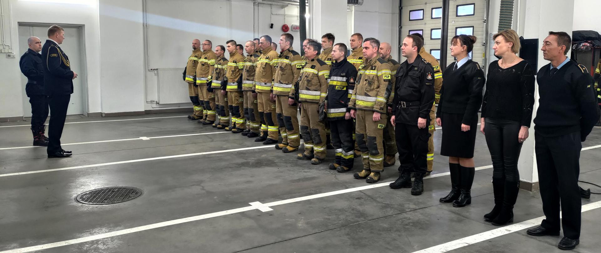 Zdjęcie przedstawia komendanta miejskiego PSP w Piekarach Śląskich oraz zastępcę dowódcy JRG stojących na przeciwko strażaków stojących w dwuszeregu.