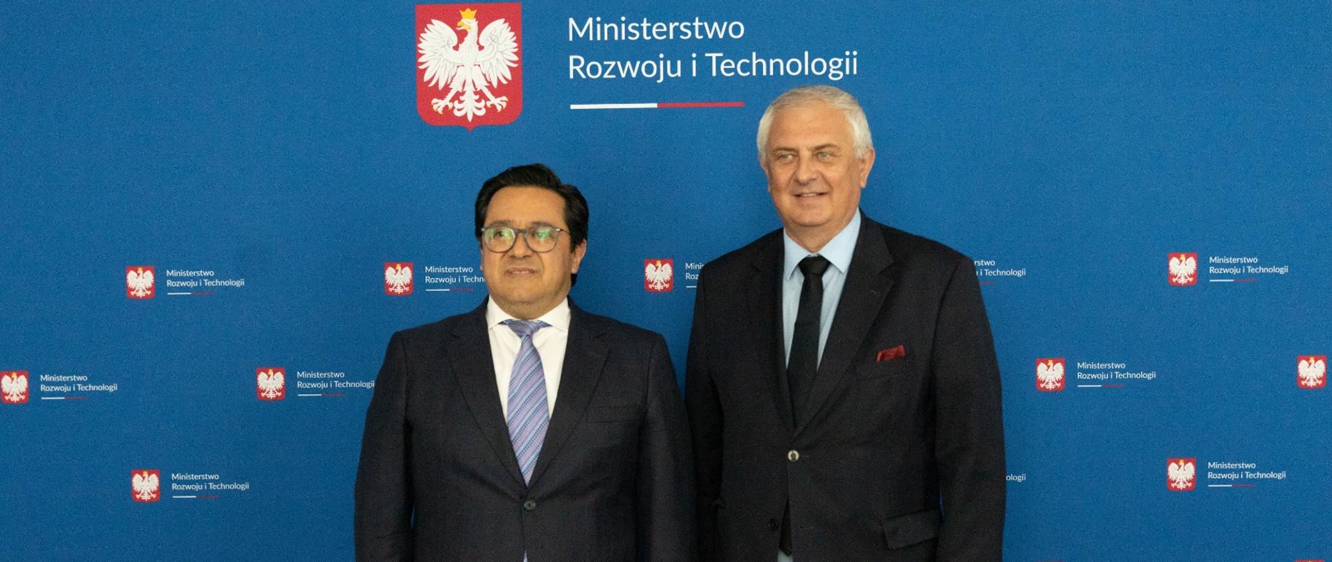 wiceminister i ambasador na tle ścianki z logo MRiT