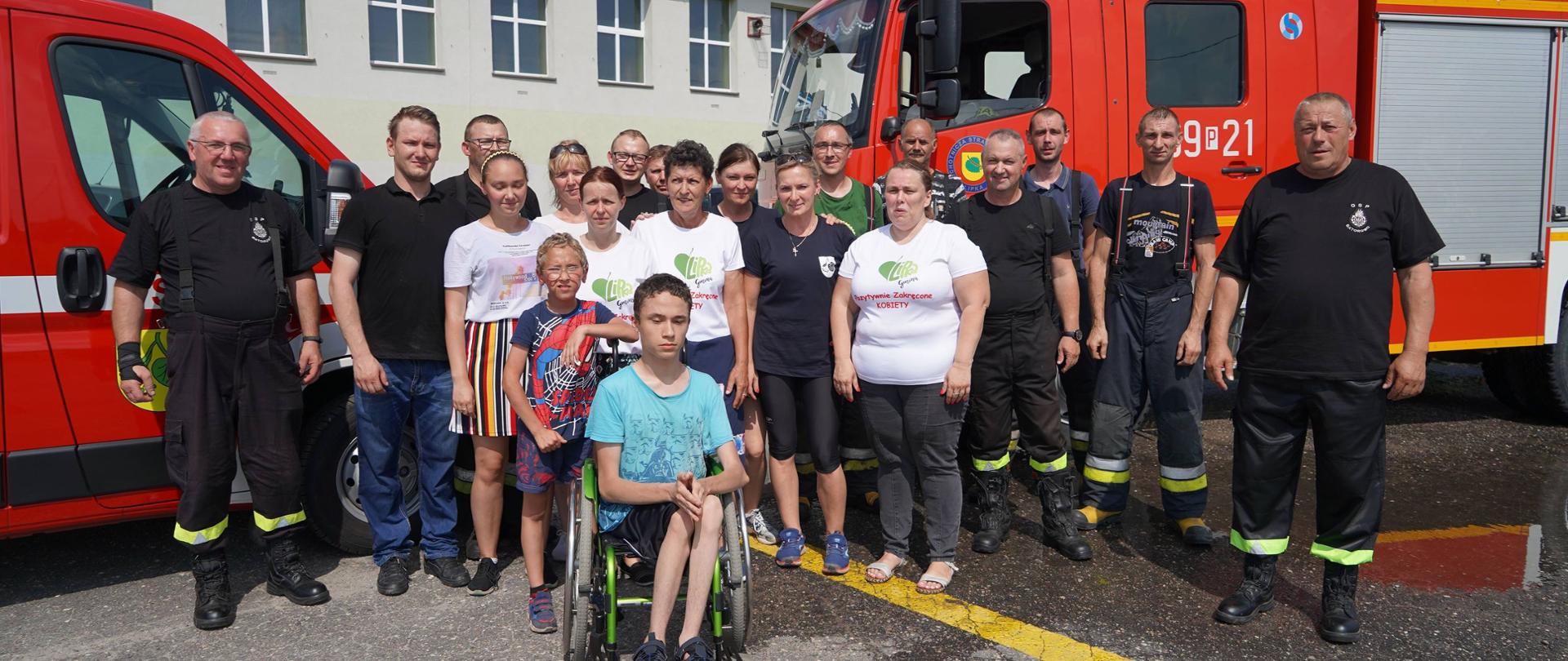 Na zdjęciu strażacy wraz z Błażejem i Miłoszem na tle dwóch samochodów strażackich. Zdjęcie grupowe. 