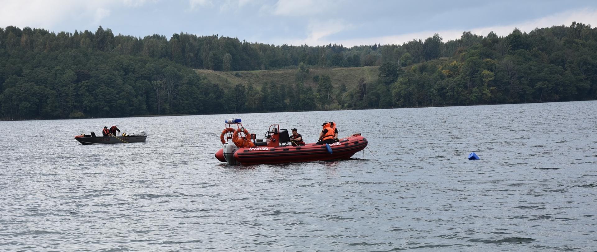 Zdjęcie obrazuje akwen z 2 łodziami i strażakami na pokładzie w tle drzewa 