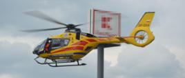 Wspólna akcja strażaków i LPR. Parking jednego z rawickich hipermarketów. W powietrze wzbija się śmigłowiec Lotniczego Pogotowia Ratunkowego. Drzwi maszyny, z lewej strony są uchylone. Widać wychylającego się członka załogi. W tle tablica reklamowa. 