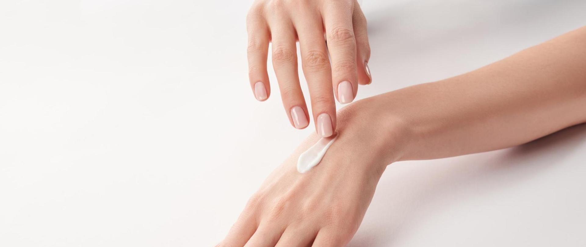 Na zdjęciu są dłonie kobiety. Jedna z nich jest posmarowana kremem.