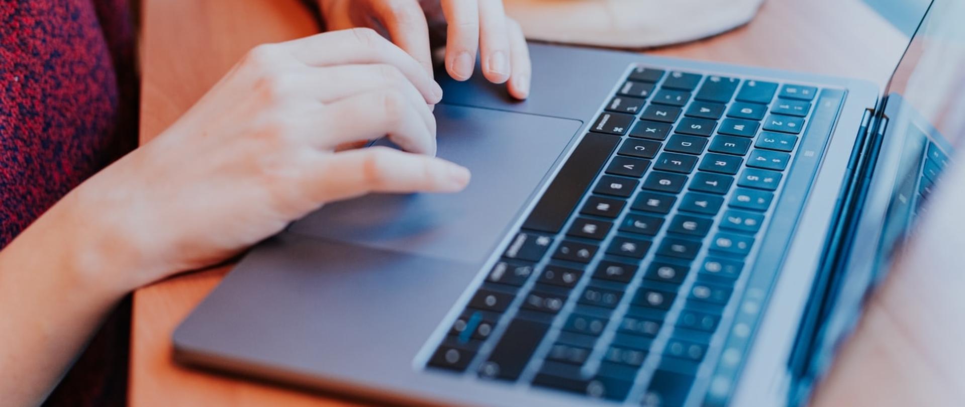 Na zdjęciu laptop i dłonie człowieka.