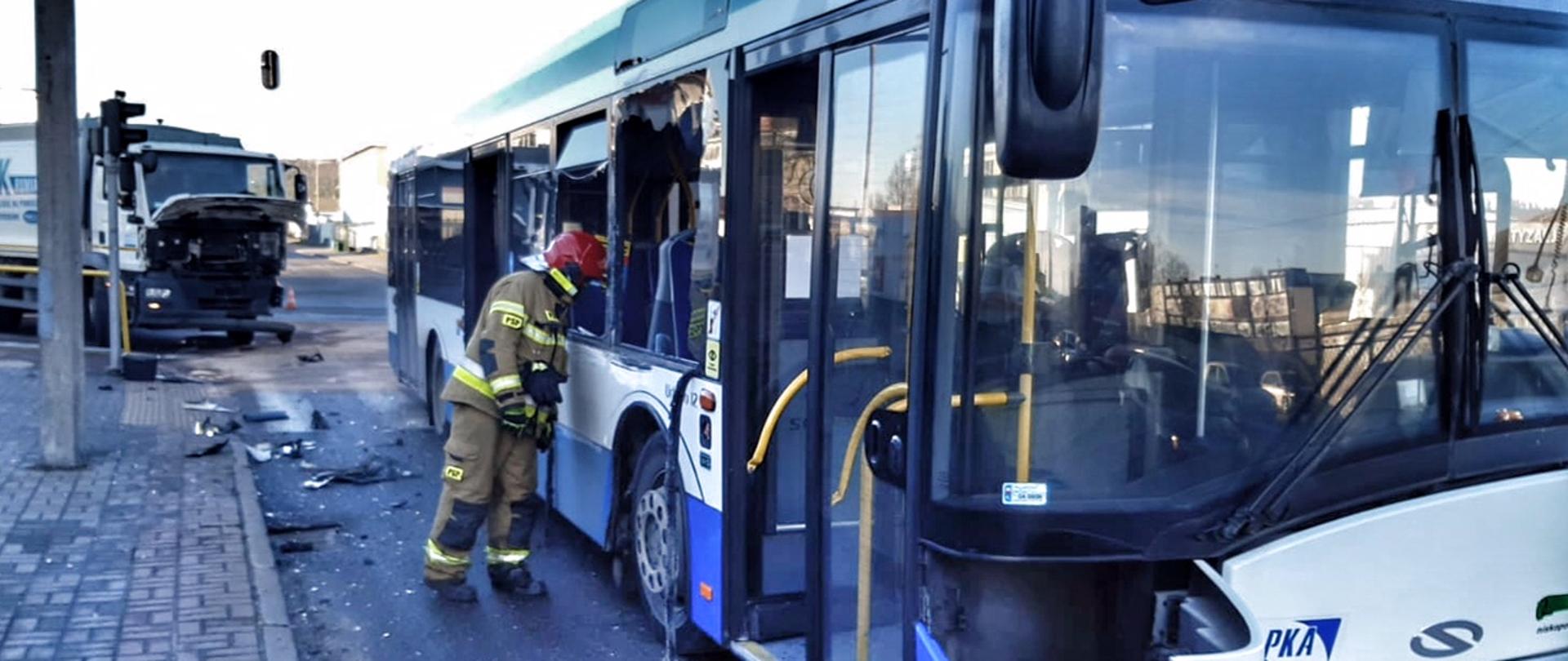 Autobus po kolizji stoi na jezdni. Za nim uszkodzone auto ciężarowe.