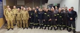 Na zdjęciu w holu Komendy Powiatowej Państwowej Straży Pożarnej w Gorlicach strażacy z Ochotniczych Straży Pożarnych i członkowie Komisji egzaminacyjnej strażacy z Państwowej Straży Pożarnej po egzaminie kończącym szkolenie dowódców OSP. Strażacy ubrani w ubrania koszarowe koloru czarnego i piaskowego bez czapek.