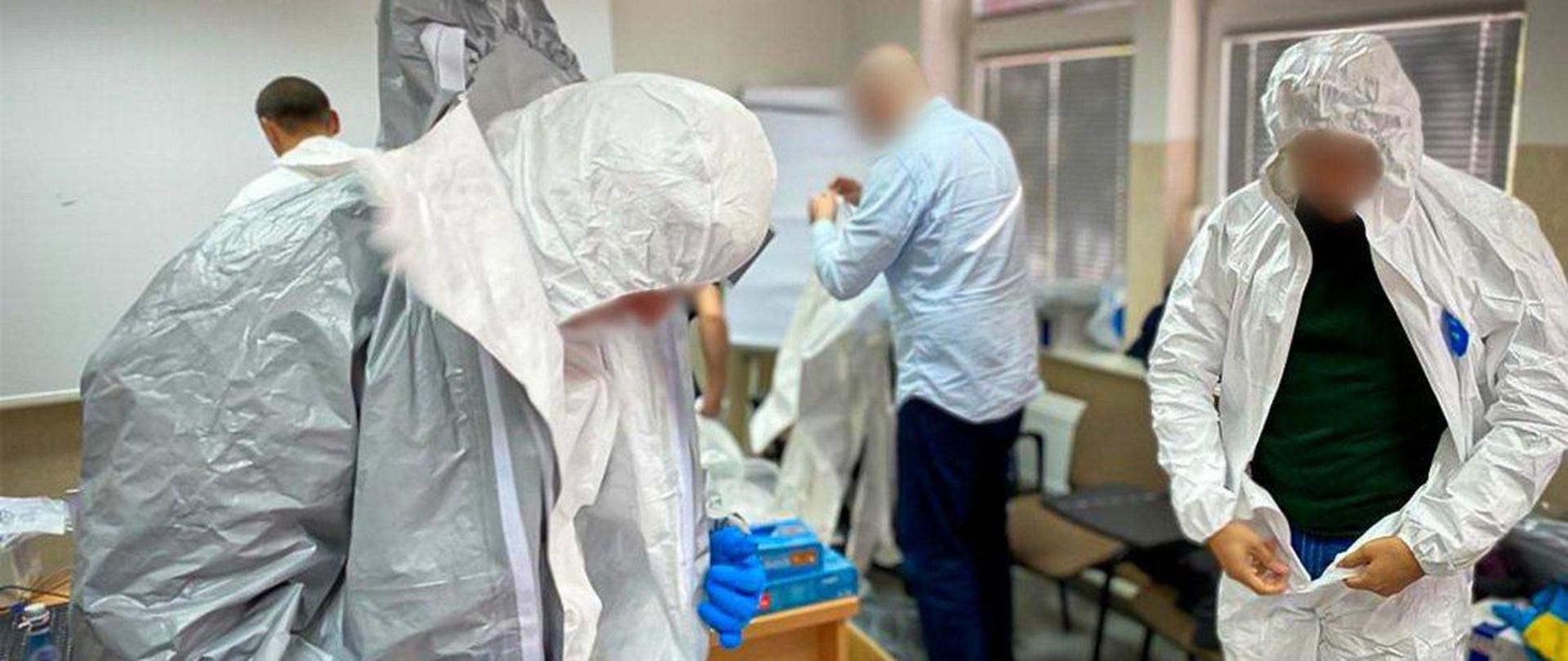 Kilka osób zakłada na siebie kombinezony ochronne.