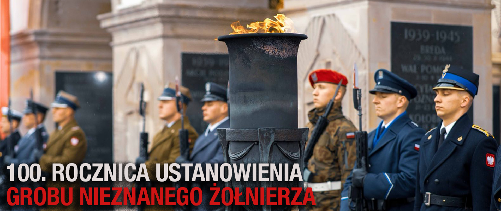 Żołnierze Wojska Polskiego, Policji, Straży Granicznej i Państwowej Straży Pożarnej stoją w uroczystym szyku przy Grobie Nieznanego Żołnierza w Warszawie. Na pierwszym planie płonie wieczny ogień w metalowym zniczu. Na dole widnieje napis: „100. rocznica ustanowienia Grobu Nieznanego Żołnierza”.