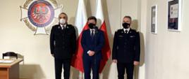 Strażacy będą wspierać akcję szczepienia przeciw COVID-19, dwóch mundurowych i minister na tle flagi.