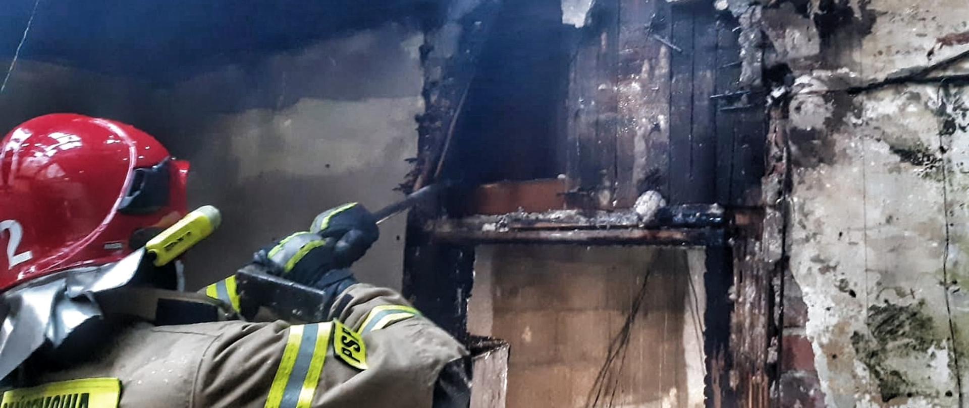 Strażak wewnątrz spalonego budynku prowadzi prace rozbiórkowe