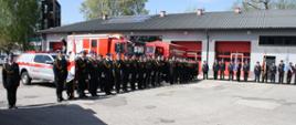 Strażacy stojący w szyku w tle pojazdy pożarnicze