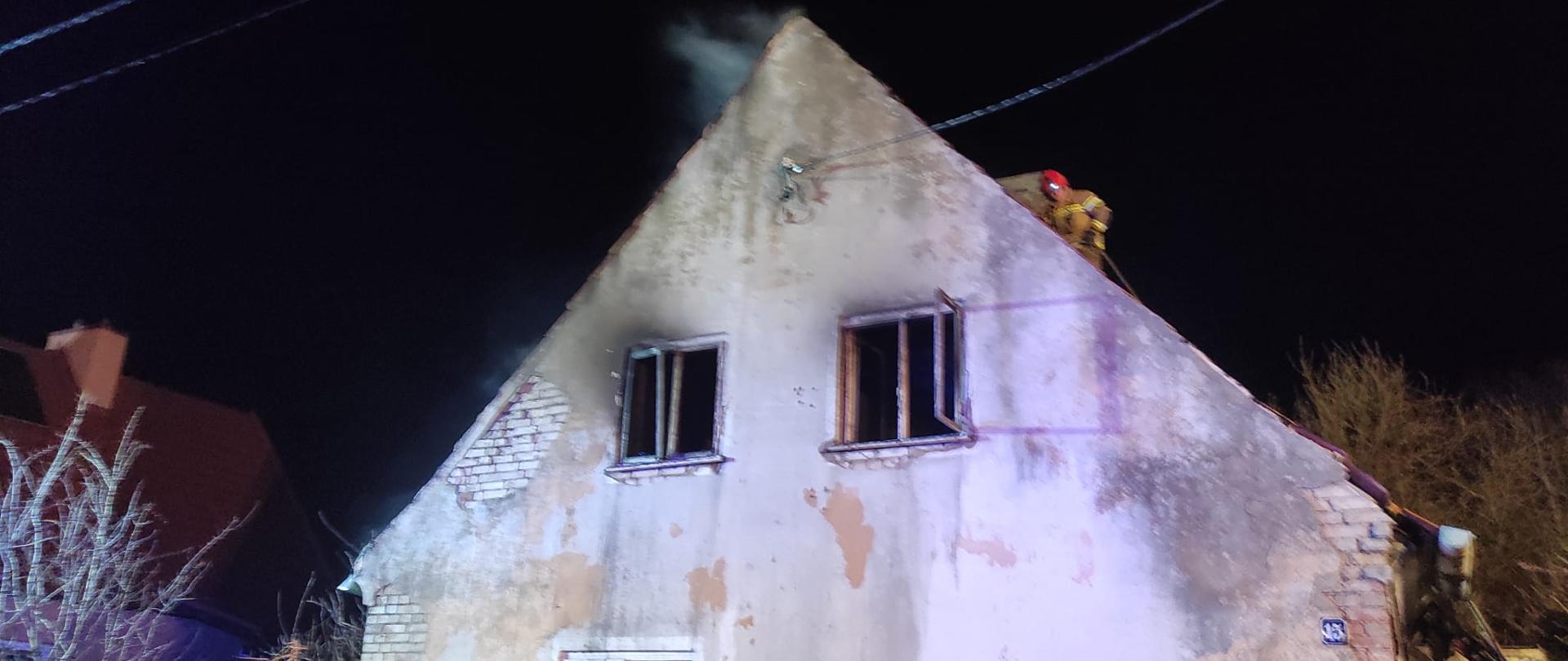 Noc. Budynek oświetlony przez światła. w budynku nie ma szyb w oknach. Obiekt po pożarze. Strażak na dachu.