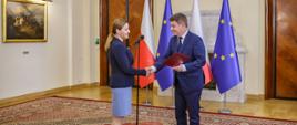 Minister Jan Grabiec wręcza akt powołania do Rady KSAP Monice Dziadkowiec, w tle flagi Polski i Unii Europejskiej
