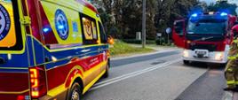 Stoi karetka pogotowia i wóz straży pożarnej z włączonymi światłami ostrzegawczymi.