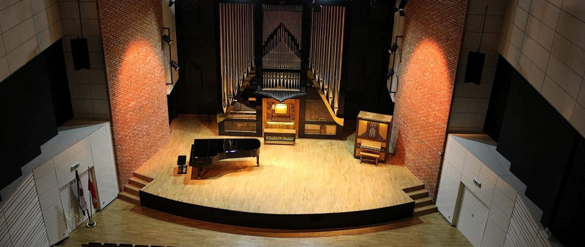 zdjęcie sali koncertowej z góry, w dolnej części widoczna widowni, na scenie organy oraz fortepian, scsena oświetlona, widownia pusta