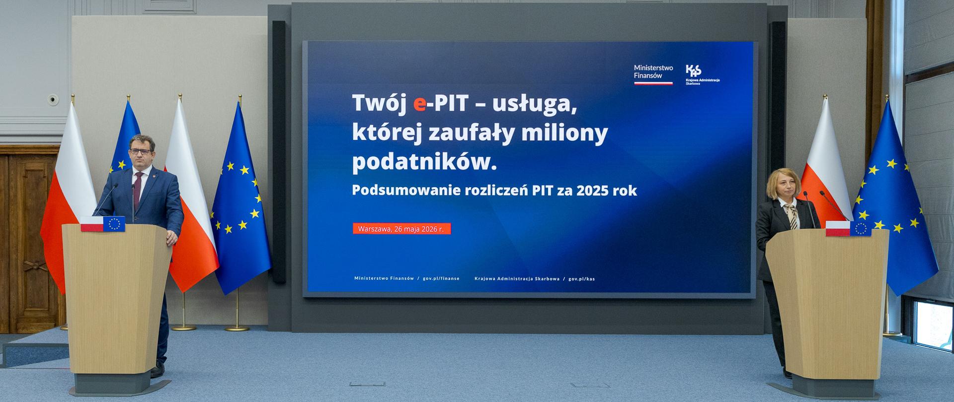 Dwie osoby stoją przy oddzielnych mównicach, a między nimi ekran z napisem „Twój e‑PIT – usługa, której zaufały miliony podatników” oraz informacją o podsumowaniu PIT za 2025 rok.