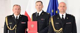 Pamiątkowe zdjęcie po wręczeniu decyzji o powołaniu na stanowisko Zastępcy Komendanta Powiatowego Państwowej Straży Pożarnej w Lęborku. Od lewej strony stoją starszy brygadier Jacek Niewęgłowski Pomorski Komendant Wojewódzki Państwowej Straży Pożarnej, po środku powołany na stanowisko starszy brygadier Tomasz Kołakowski , obok niego brygadier Leszek Formela Komendant Powiatowy Państwowej Straży Pożarnej w Lęborku. Powołany na stanowisko trzyma w dłoniach czerwone teczkę z dokumentami. W tle widoczna flaga państwowa oraz flaga Unii Europejskiej. 