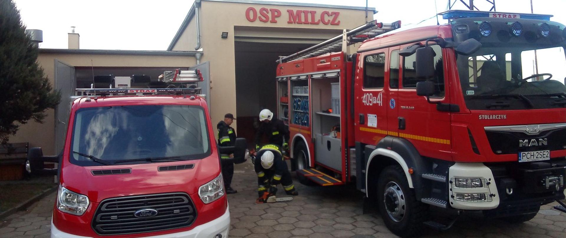 Zdjęcie przedstawia strażaków sprawdzających sprzęt strażacki podczas jesiennych przeglądów technicznych oraz samochody gaśnicze.
W tle budynek remizy OSP.

