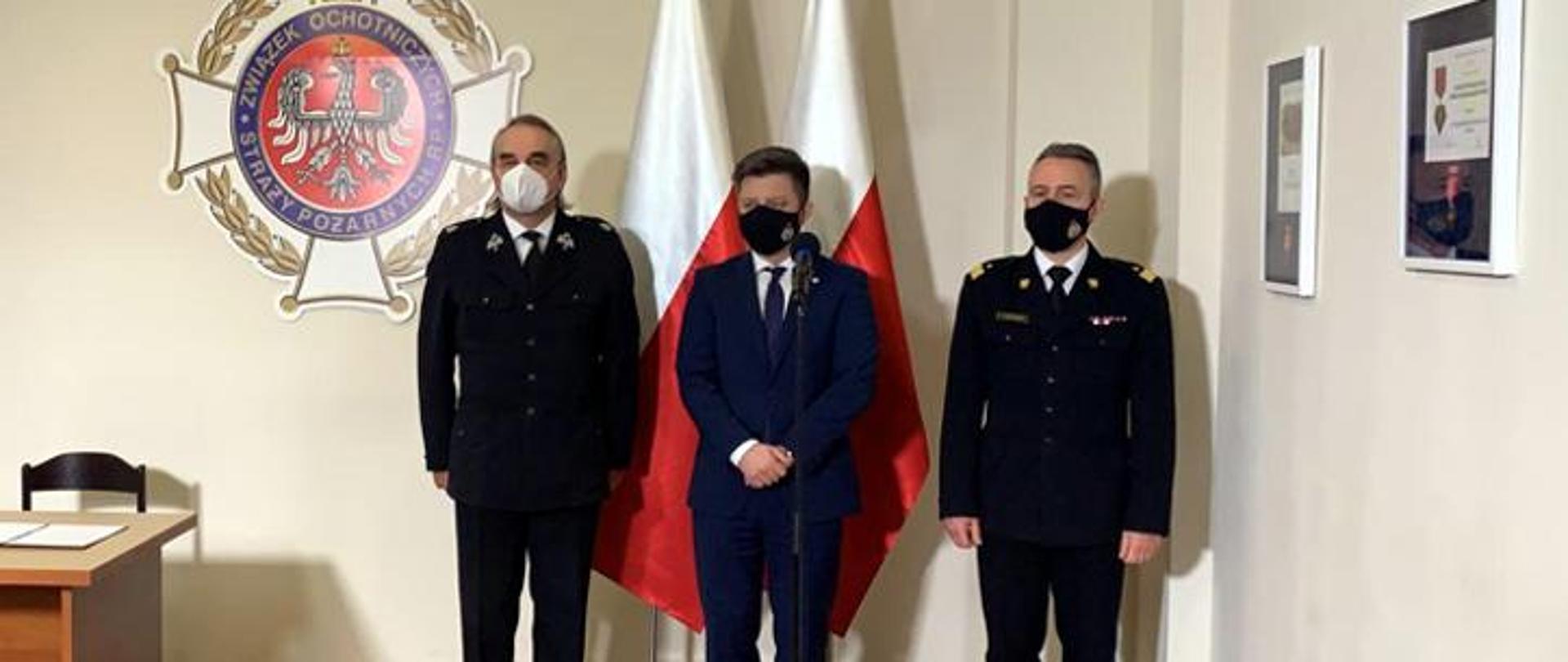 na zdjęciu na tle narodowych flag stoją od lewej: dh. Waldemar Pawlak prezes ZG ZOSP RP.,Michał Dworczyk szef Kancelarii Prezesa Rady Ministrów, nadbryg. Andrzejem Bartkowiakiem, komendant główny PSP 