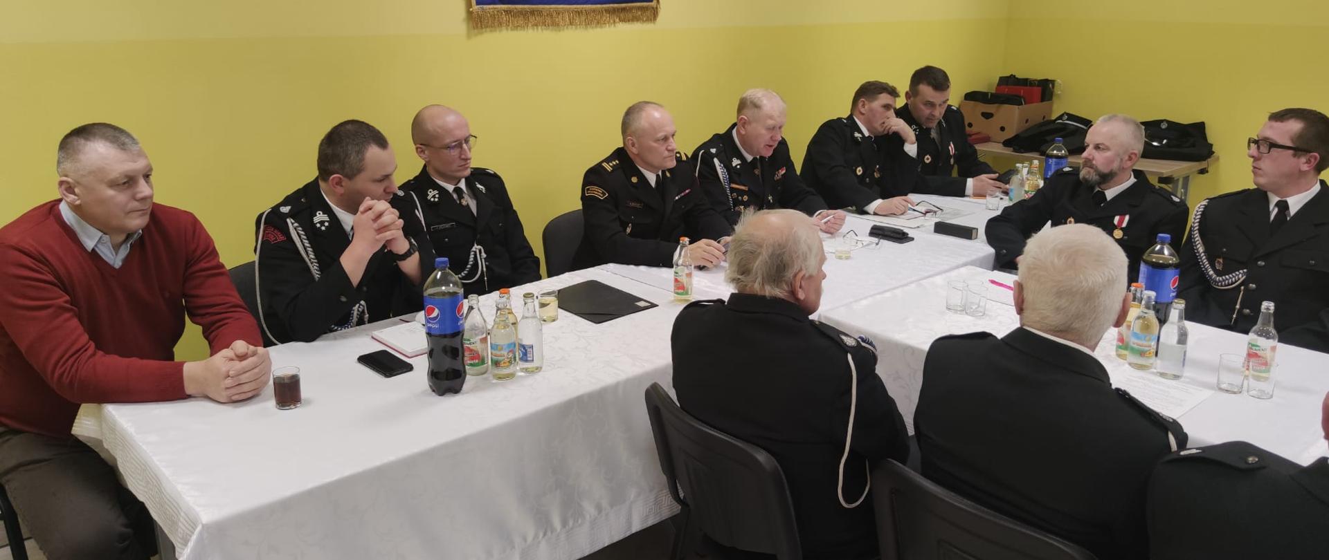 Na zdjęciu widać druhów OSP w mundurach strażackich siedzących przy stole w remizie OSP Garbacz. Przy stole siedzą również Komendant Powiatowy PSP w Ostrowcu Św, oraz Wójt Gminy Waśniów.