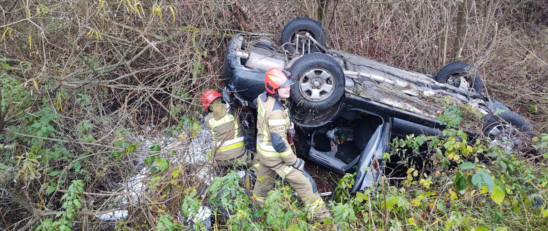 Samochód osobowy na dachu a obok strażacy.