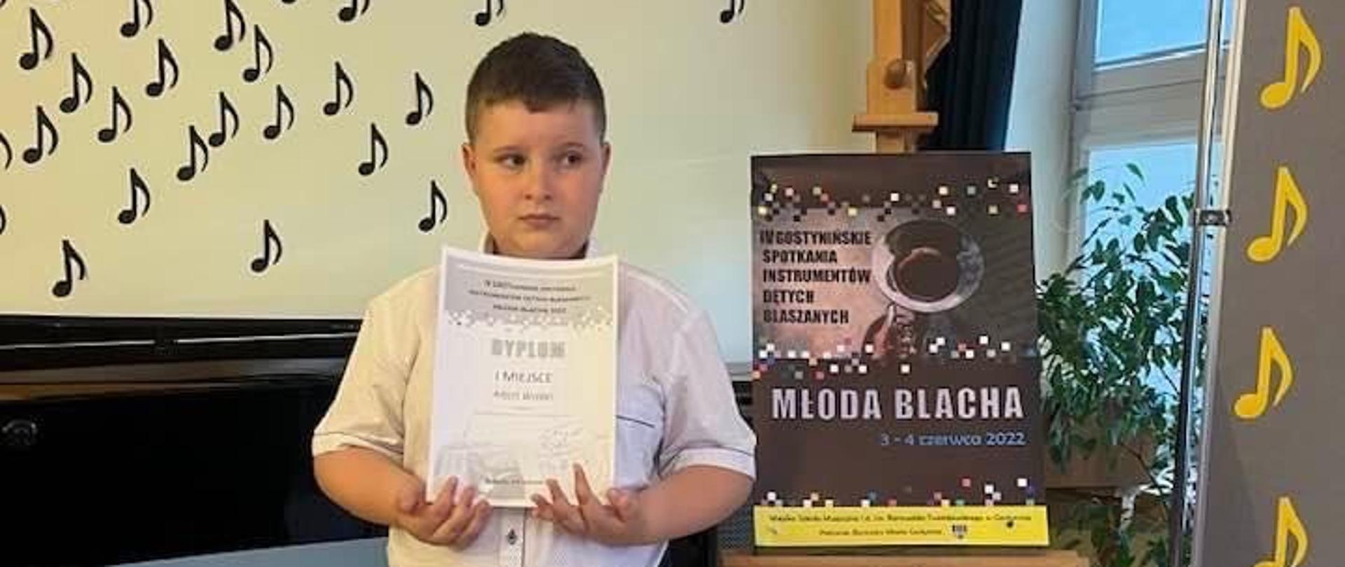 Chłopiec stoi z dyplomem, obok sztaluga z plakatem.