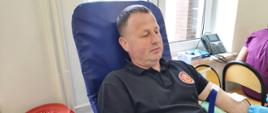 Na zajęciu widoczny mężczyzna siedzący na fotelu na sali oddający krew podczas akcji zbiórki krwi zorganizowanej przez Klub Honorowych Dawców Krwi Polskiego Czerwonego Krzyża przy Komendzie Powiatowej Państwowej Straży Pożarnej w Gorlicach i Klub Honorowych Dawców Krwi Polskiego Czerwonego Krzyża Moszczenica.