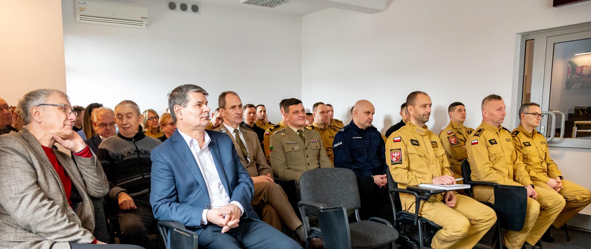 Zaproszeni goście i funkcjonariusze znajdują się na świetlicy i słuchają prezentacji. 