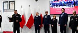 Pomorski komendant wojewódzki Państwowej Straży Pożarnej przemawia, za ni stoją zaproszeni goście.