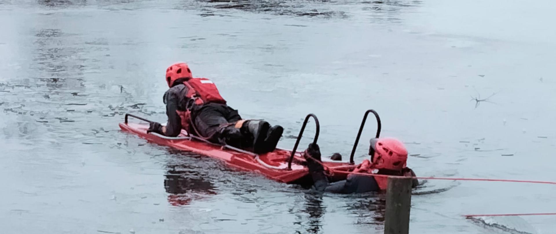 Fotografia przedstawia dwóch strażaków w wodzie podczas ćwiczeń ratownictwa lodowego