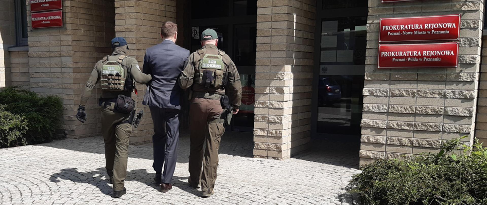 Funkcjonariusze Służby Celno-Skarbowej przed wejściem do Prokuratury, prowadzą zatrzymanego.