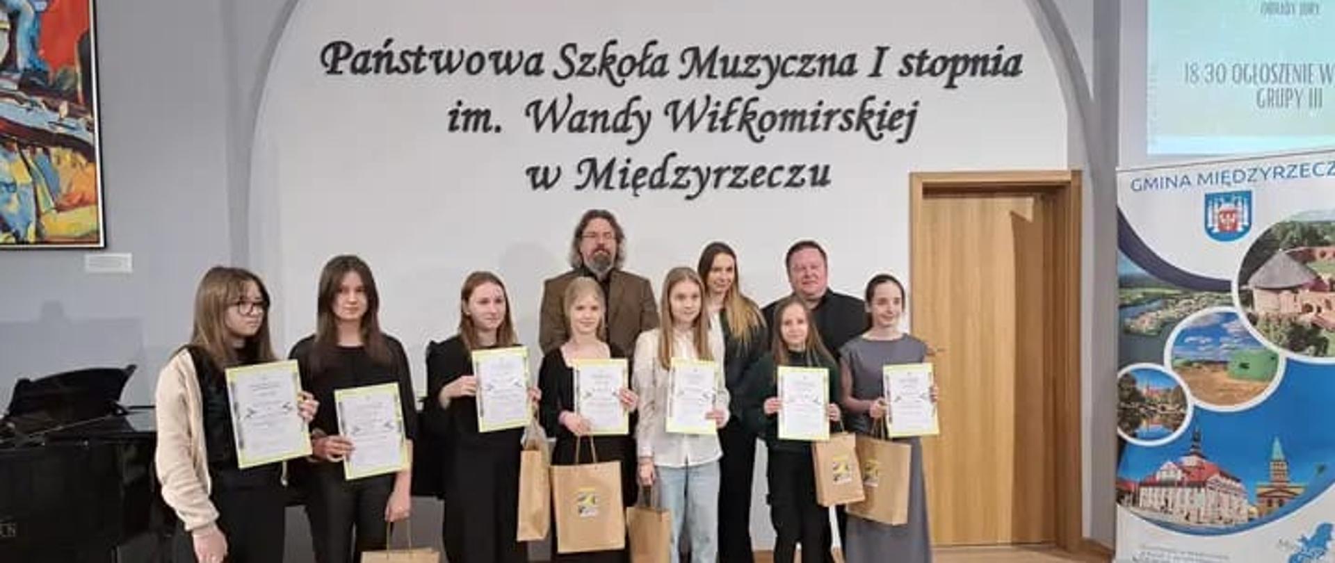 Laureaci konkursu smyczkowego oraz jurorzy stoją z dyplomami na scenie szkoły muzycznej w Międzyrzeczu