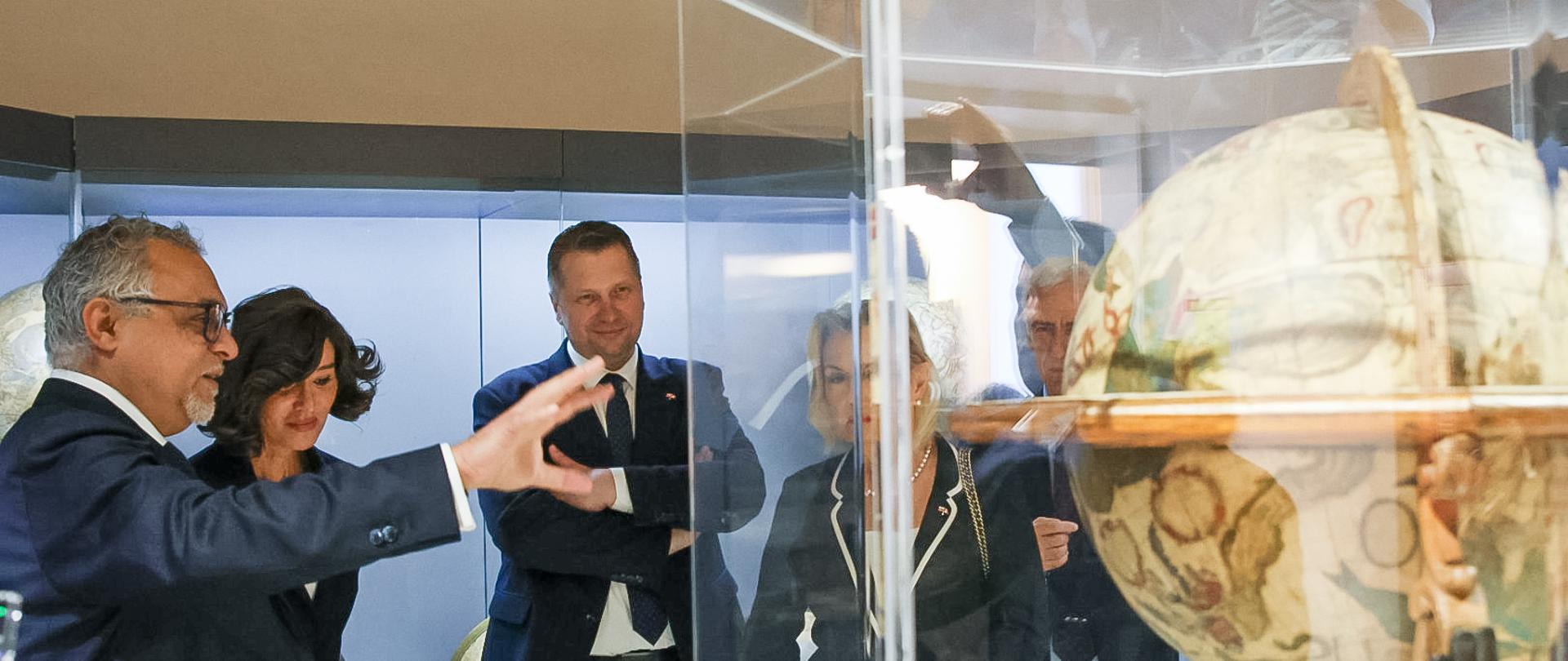 Minister Czarnek, minister Berninini i ambasador Andres oglądają duży globus w szklanej gablocie. Na pierwszym planie mężyczyzna wskazujący na eksponat. 