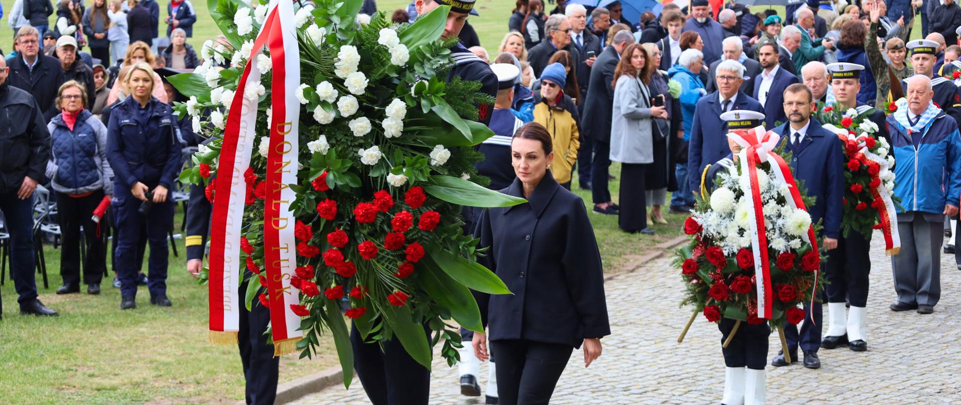 marynarz niesie wieniec, za nim idzie kobieta