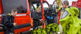 Strażacy - funkcjonariusze specjalistycznej grupy ratownictwa chemiczno-ekologicznego zakładają sprzęt ochronny i sprzęt łączności przystosowany do pracy w strefach niebezpiecznych.