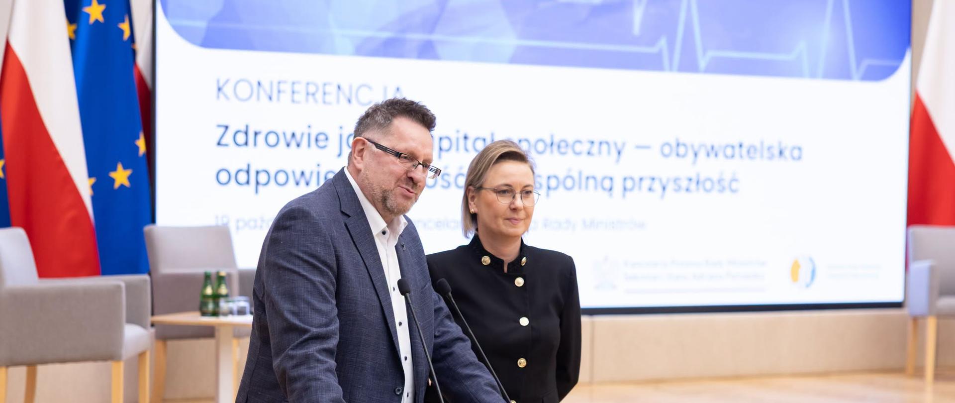 Konferencja „Zdrowie jako kapitał społeczny – obywatelska odpowiedzialność za wspólną przyszłość”, Kancelaria Prezesa Rady Ministrów. Na zdjęciu Pani Minister Adriana Porowska, Sekretarz Stanu w KPRM, Wiceprzewodnicząca Komitetu do spraw Pożytku Publicznego i ks. dr Arkadiusz Nowak, Prezes Instytutu Praw Pacjenta i Edukacji Zdrowotnej przemawiają do uczestników spotkania podczas uroczystego otwarcia spotkania. W tle widoczny ekran z tytułem konferencji oraz fragmenty flagi Polski i Unii Europejskiej.