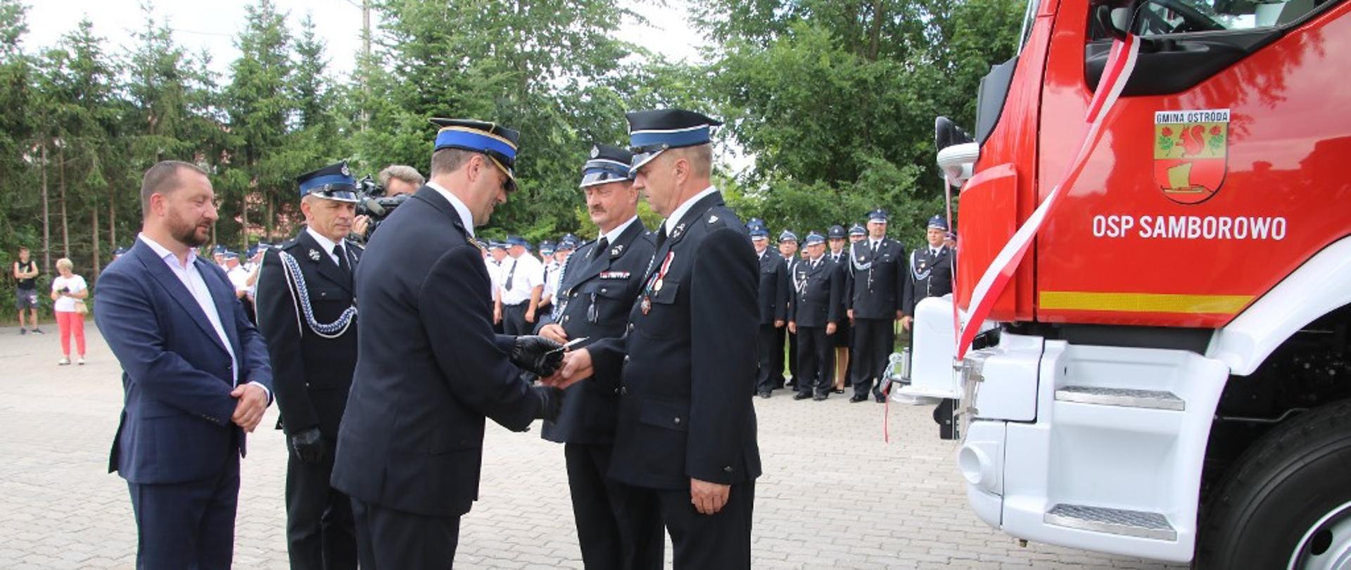Zastępca Komendanta Wojewódzkiego PSP w Olsztynie wręcza kluczyki do nowego samochodu pożarniczego. 