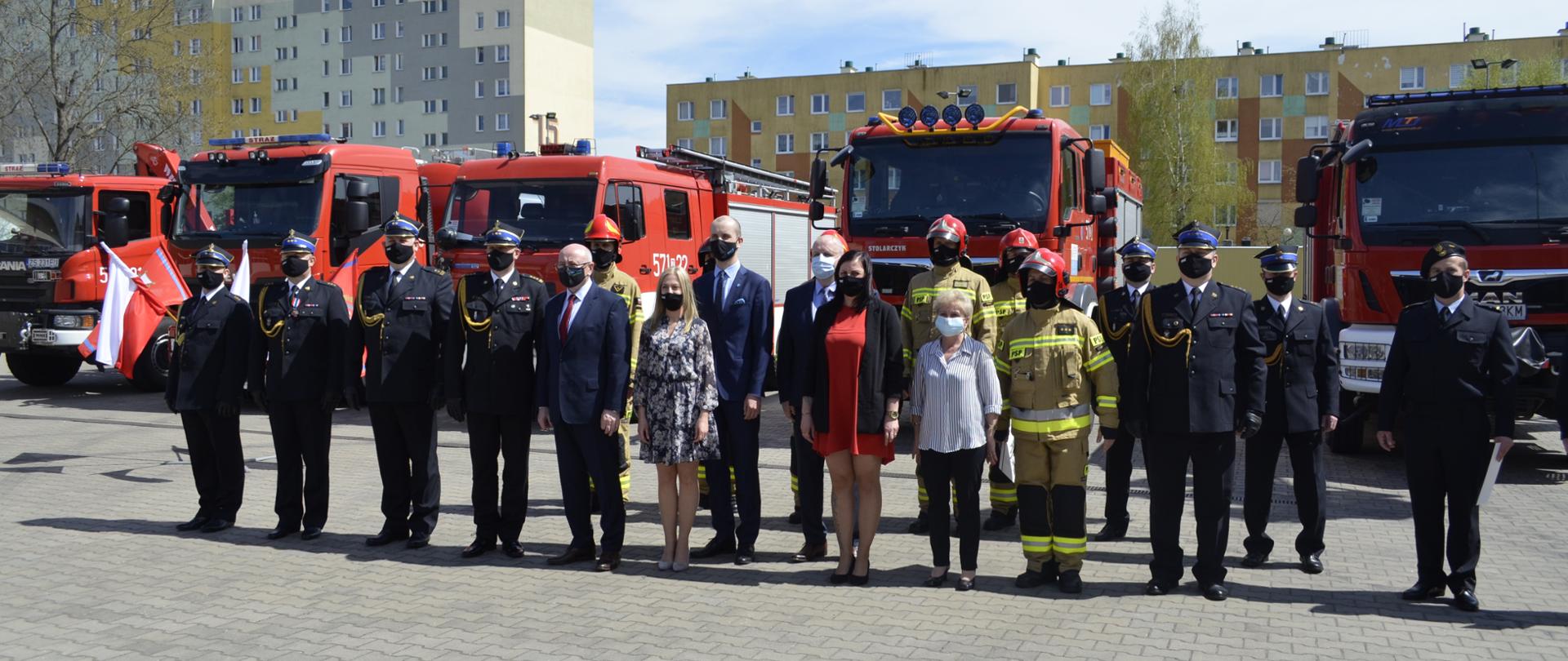 Zdjęcie przedstawia strażaków, pracowników cywilnych oraz zaproszonych gości na tle samochodów pożarniczych
