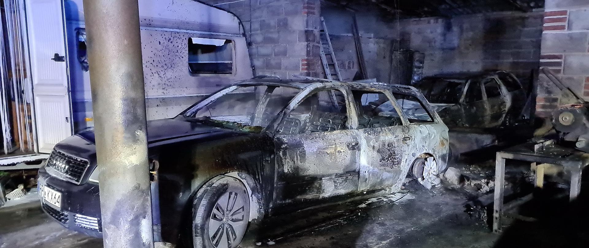 Dwa spalone auta osobowe w tle nadpalona przyczepa kempingowa