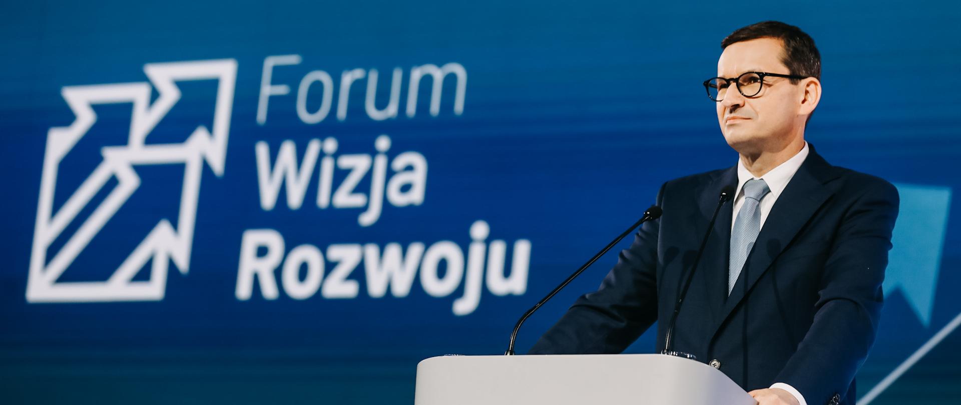 Premier Mateusz Morawiecki stoi przed mównicą a w tle plansza z napisem Forum Wizja Rozwoju.