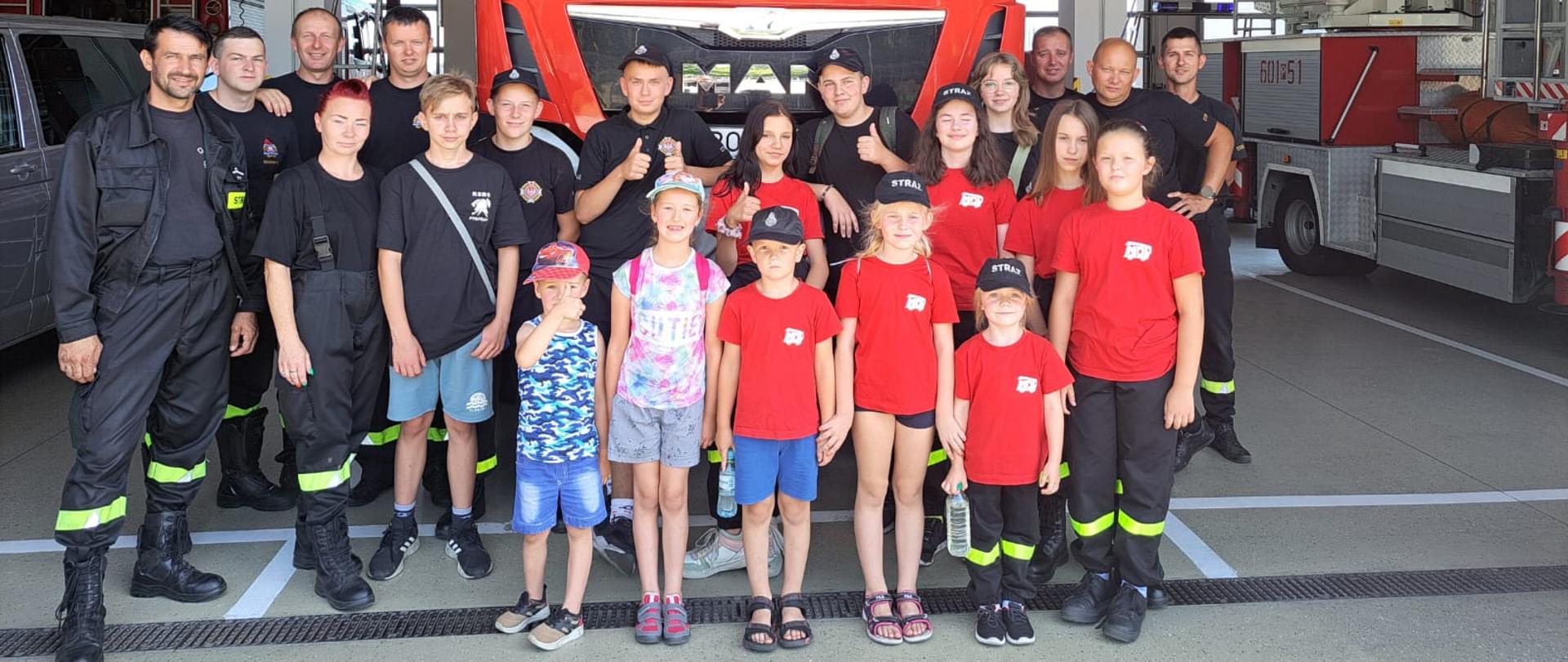 Zdjęcie grupowe MDP z opiekunami z OSP Pysząca i strażakami JRG Śrem na tle samochodu ratowniczo - gaśniczego