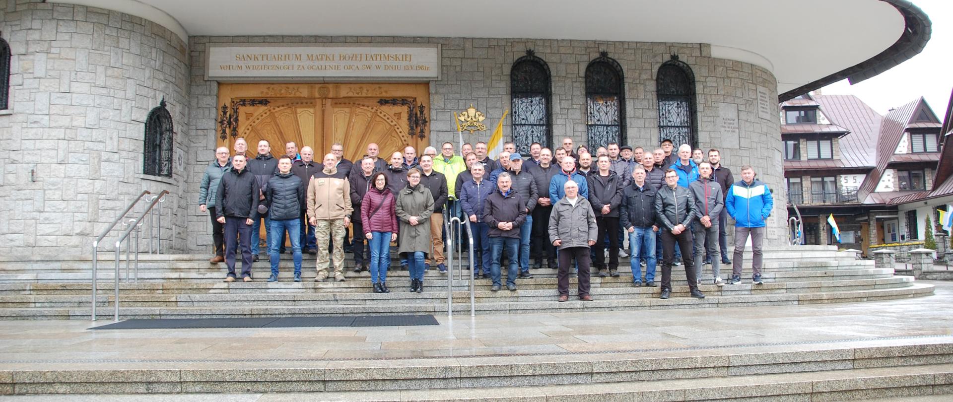 W centralnej części zdjęcia grupa ludzi na tle budynku kościoła