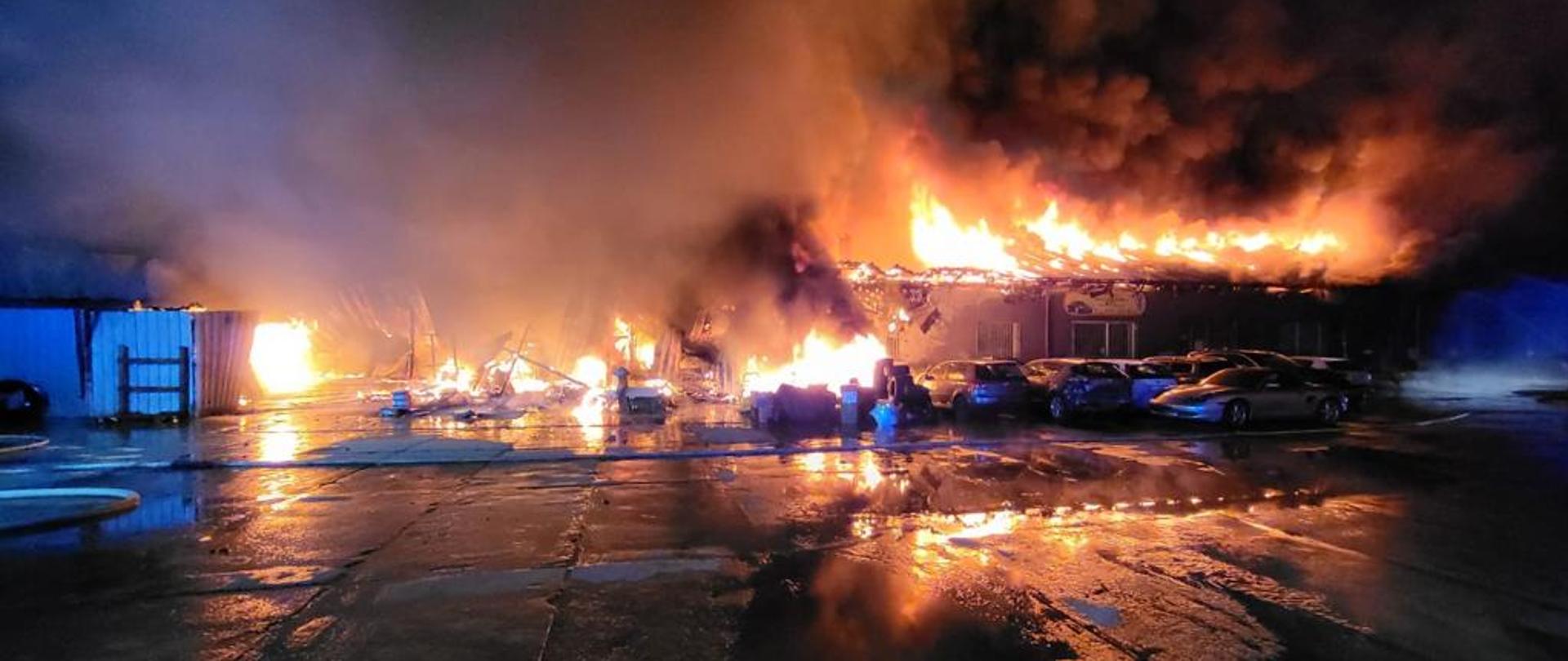 Widać pożar budynku lakierni, są płomienie, pożar rozwinięty, przed budynkiem kilka samochodów 