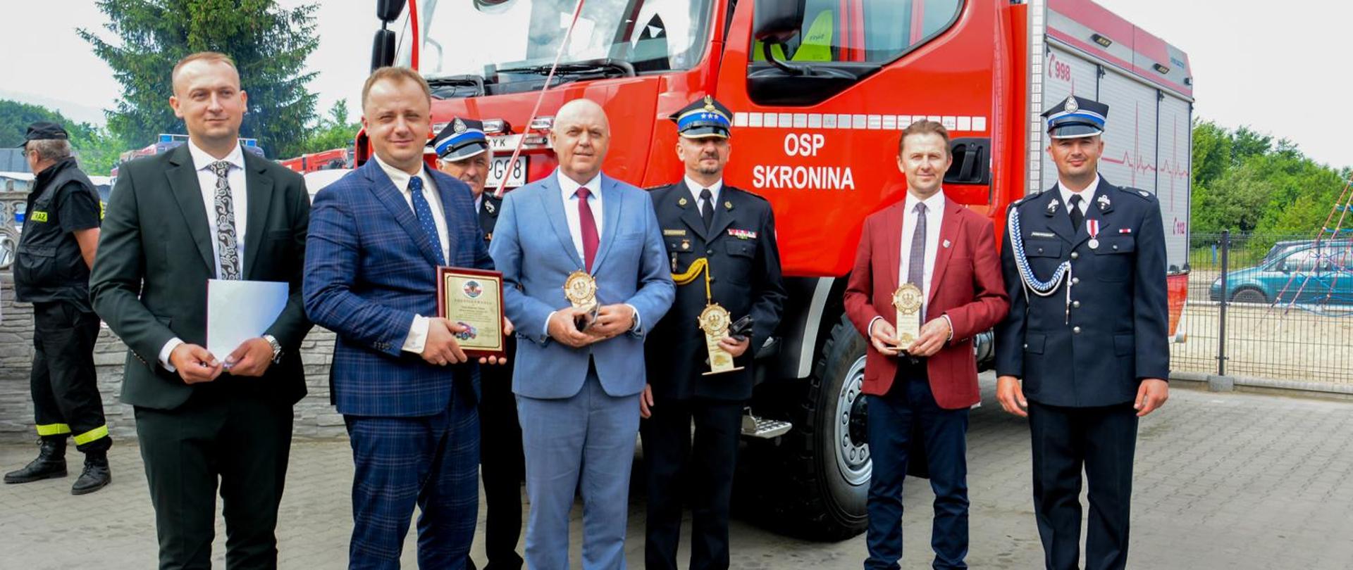 druhowie, strażacy i politycy pozują do zdjęcia na tle samochodu gaśniczego