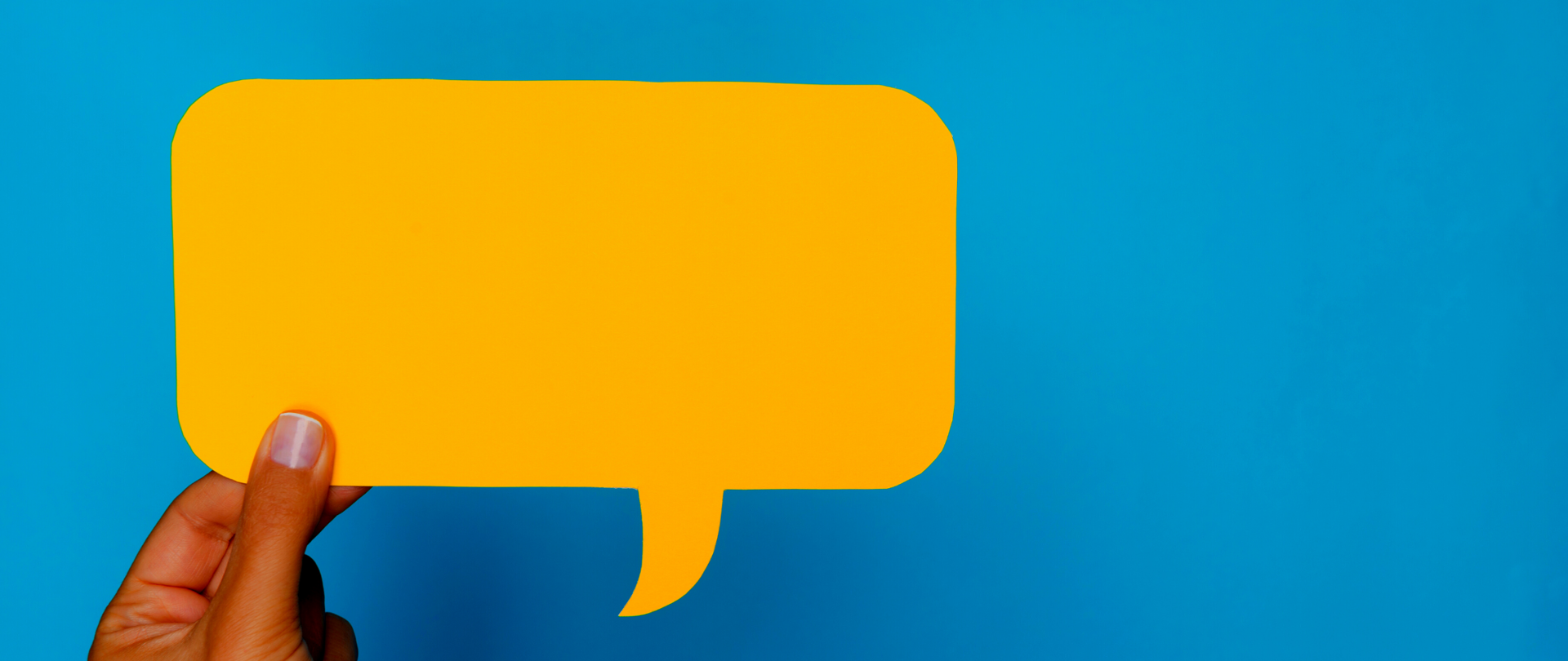 Zdjęcie - symbolizująca komentarz/opinię żółta chmurka na niebieskim tle. Z lewej strony widoczne palce dłoni trzymającej chmurkę.