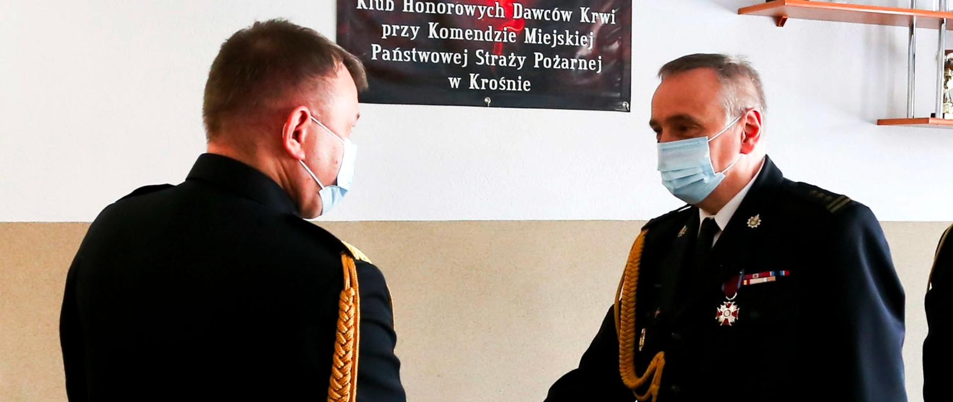 Zdjęcie przedstawia Pana st. bryg. Mariusza Bieńczaka składającego meldunek o zdaniu obowiązków Komendanta Miejskiego Państwowej Straży Pożarnej w Krośnie Podkarpackiemu Komendantowi Wojewódzkiemu PSP. Obydwaj funkcjonariusze w mundurach galowych stoją zwróceni do siebie twarzami.