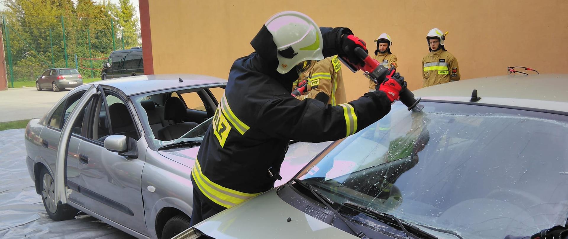 Strażak wycina przednia szybę w samochodzie przy użyciu elektronarzędzia