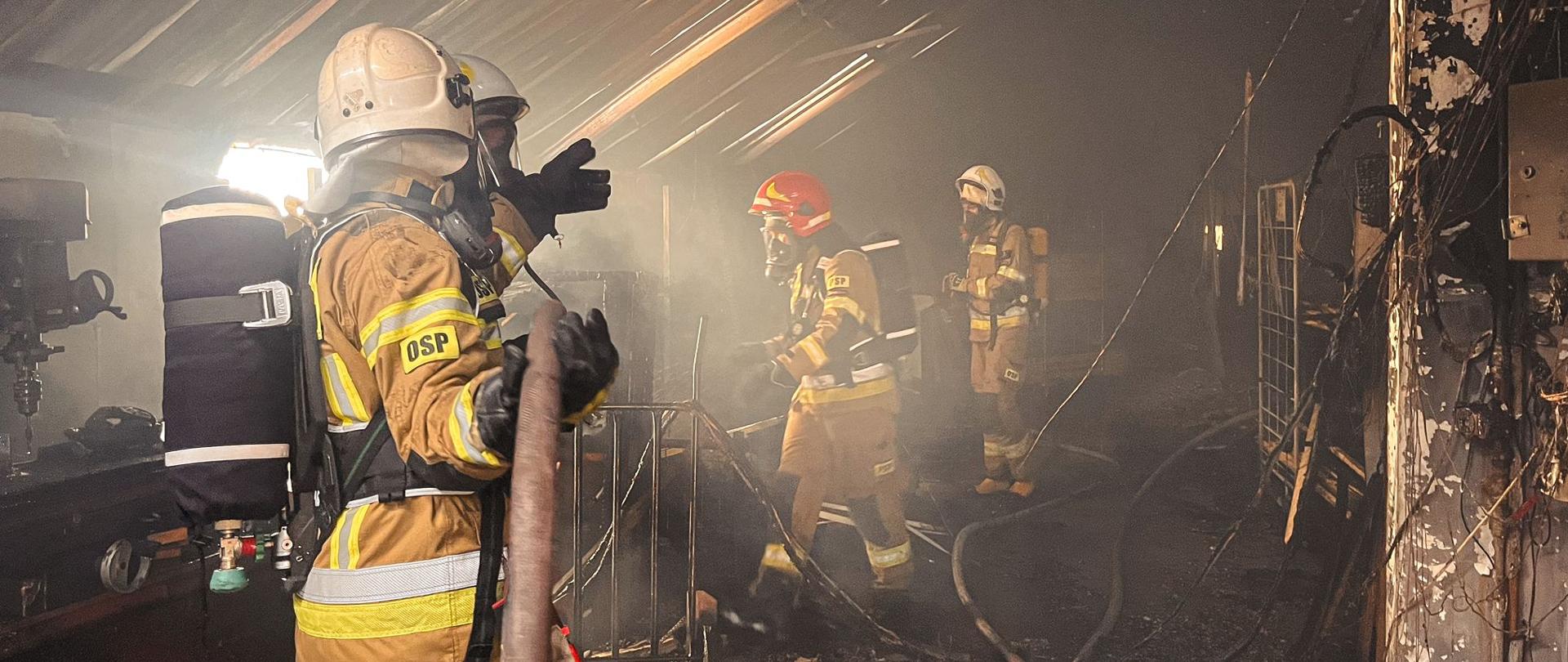 Strażacy wewnątrz budynku podczas prowadzenia działań gaśniczych.