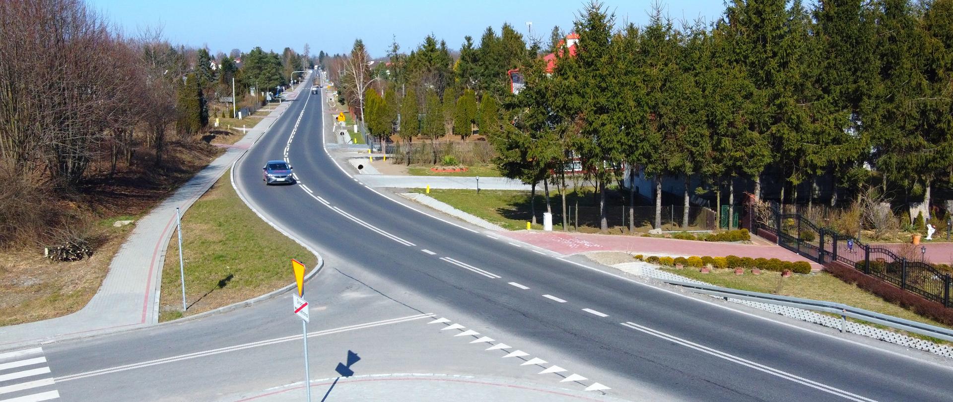 widok drogi numer 77 biegnącej przez miejscowość Pełkinie, świeci słońce, jadą samochody